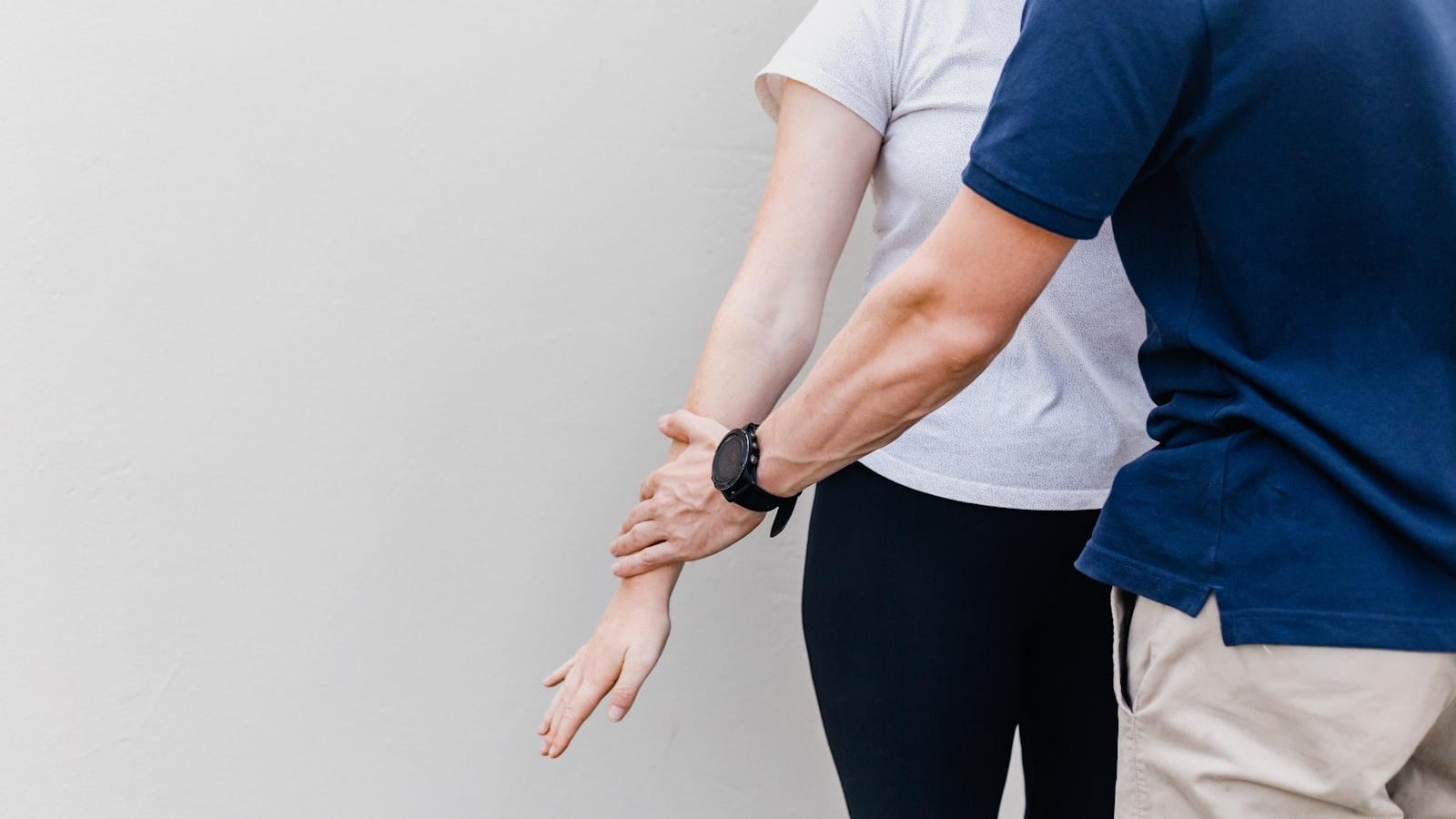 Close-up of a clinician palpating a patient's wrist and forearm against a clean studio-grey wall