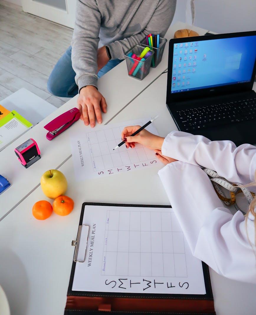 A dietitian filling out a weekly meal plan with a client at a clinic desk