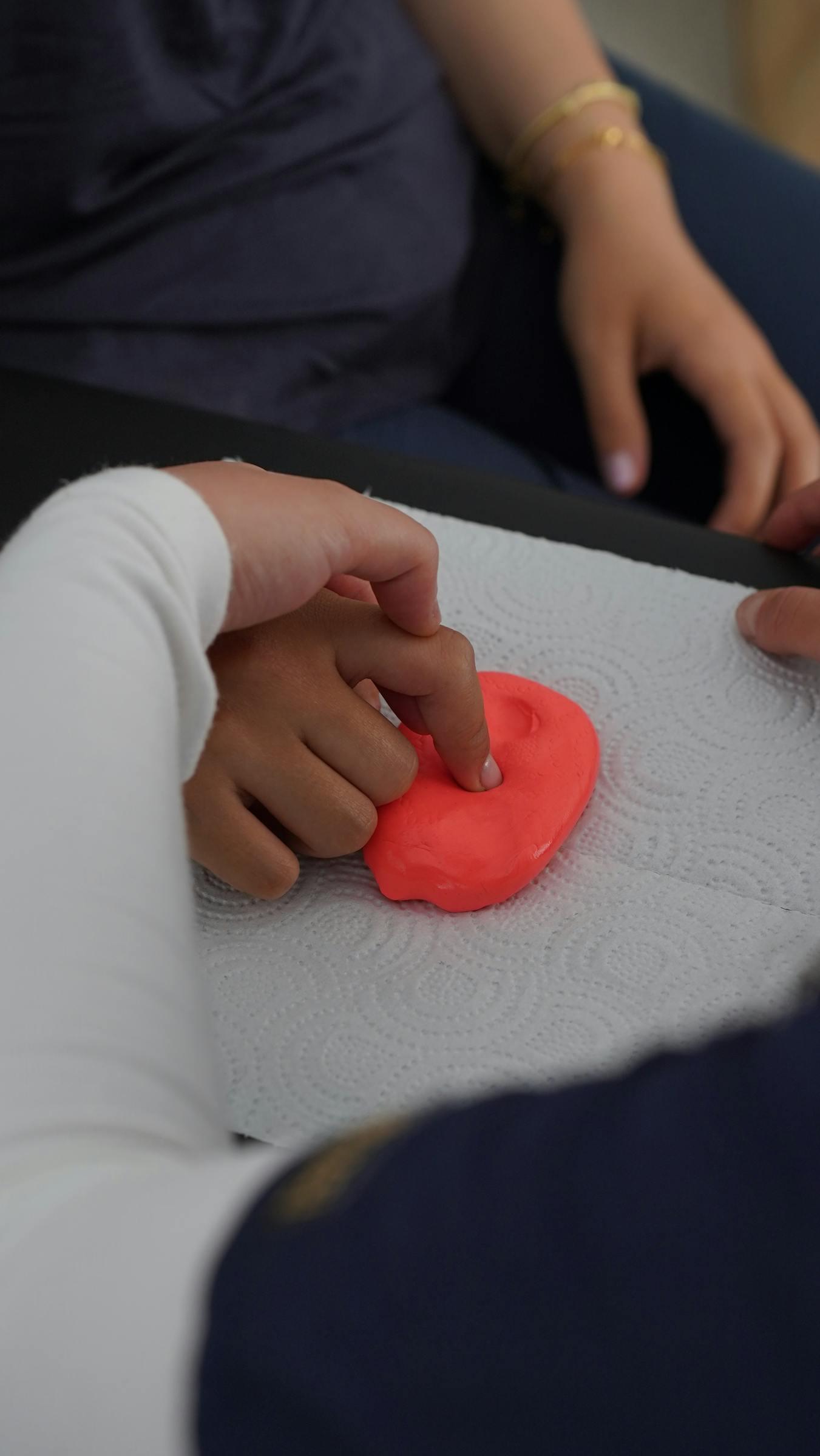 Close-up of two pairs of hands shaping red therapy putty during a hand-therapy session