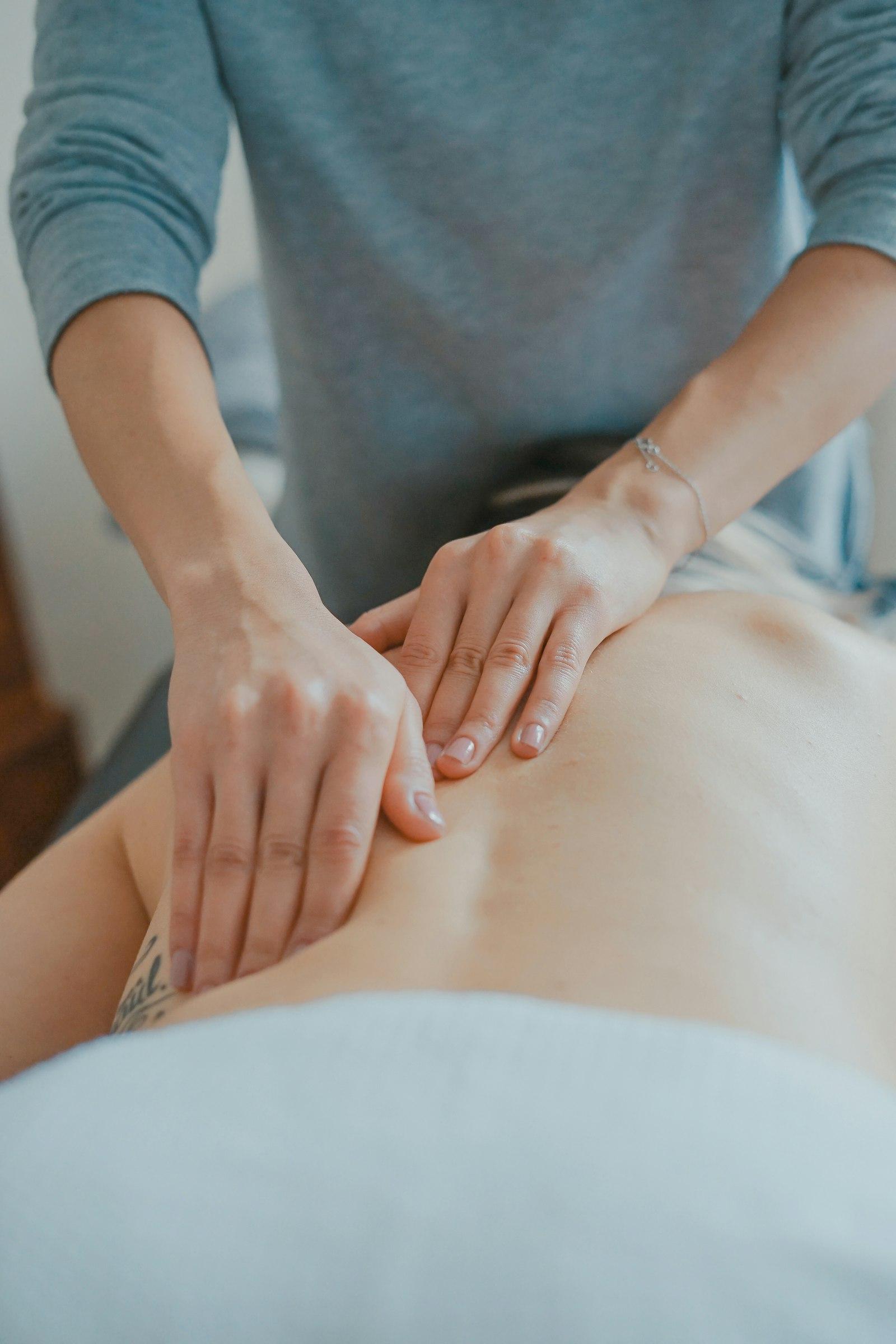 A therapist's hands applying focused soft-tissue pressure to a patient's upper back