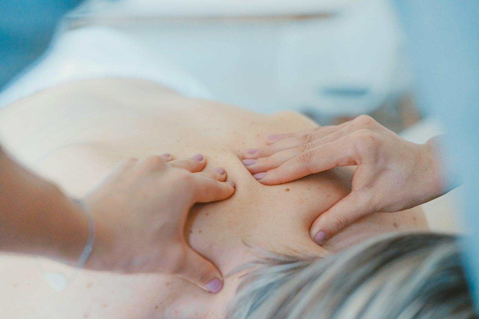 A remedial therapist's hands working a trigger point between a client's shoulder blades