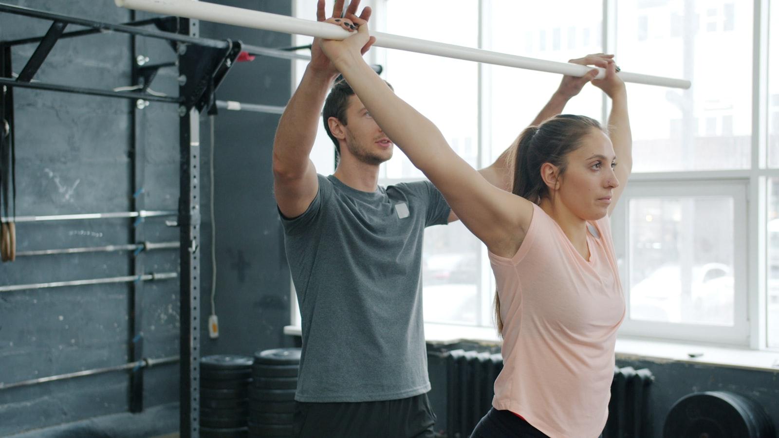 A clinician spotting a patient through a supervised overhead bar mobility drill in a clinical rehab gym